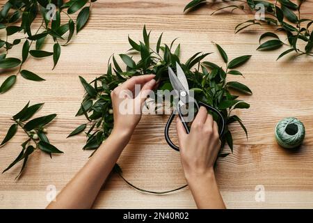 Florist macht wunderschönen Mistelkranz am Holztisch, Draufsicht. Traditionelle Weihnachtsdekor Stockfoto