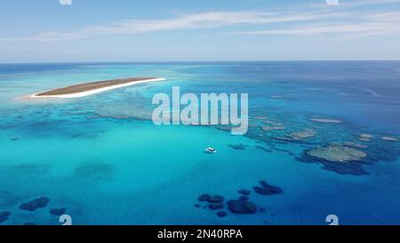 Luftaufnahme eines Segelboots, das in einer klaren Lagune mit einer tropischen Insel dahinter vor Anker liegt, umgeben von einem Riff am Great Barrier Reef Stockfoto