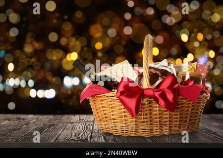 Korb aus Korb voller Geschenke auf Holztisch vor verschwommenem weihnachtlichem Licht. Platz für Text Stockfoto