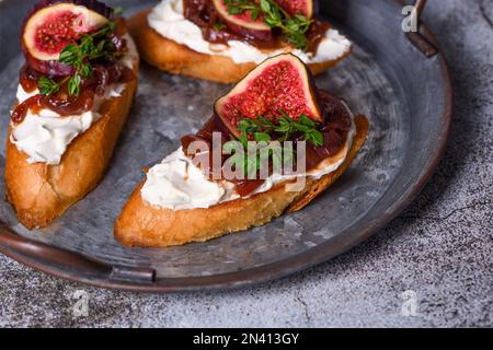 Cannapé oder Crostini mit geröstetem Baguette, Frischkäse, Zwiebelmarmelade, Feigen und frischem Thymian auf einer Dose. Ideale Vorspeise als Aperitif. Stockfoto