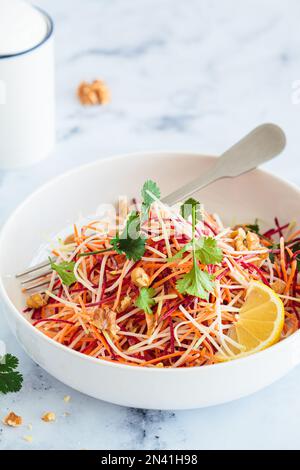 Frühlingsmöhren, Rüben, Kohlsalat mit Nüssen und Kräutern in einer weißen Schüssel. Stockfoto