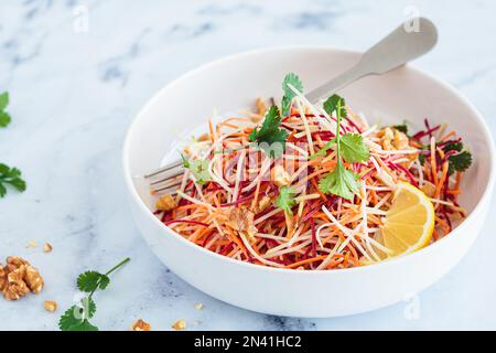 Frühlingsmöhren, Rüben, Kohlsalat mit Nüssen und Kräutern in einer weißen Schüssel. Stockfoto