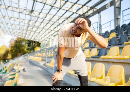Müde hispanische Athleten, die sich nach dem Joggen gebeugt und atmet, Mann, der an sonnigen Tagen Sport treibt, mit aktiven Übungen und Fitness, Sportler, der sich nach dem Joggen ausruht. Stockfoto