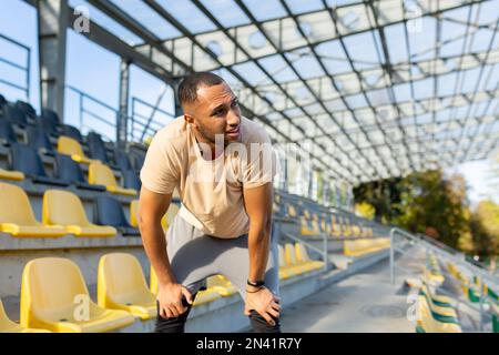 Müde hispanische Athleten, die sich nach dem Joggen gebeugt und atmet, Mann, der an sonnigen Tagen Sport treibt, mit aktiven Übungen und Fitness, Sportler, der sich nach dem Joggen ausruht. Stockfoto
