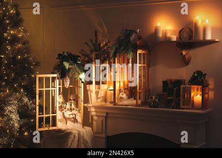 Wunderschöne Holzlaternen und andere Dekorationen auf Kaminsims im Zimmer mit Weihnachtsbaum Stockfoto