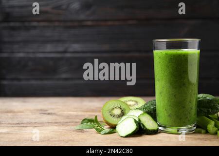 Köstlicher grüner Saft und frische Zutaten auf einem Holztisch vor schwarzem Hintergrund. Platz für Text Stockfoto