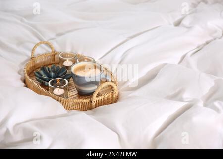 Weidenschale mit Tasse Kaffee und Kerzen auf weicher weißer Decke Stockfoto