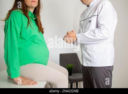 Der Arzt berät ein schwangeres Mädchen vor der Geburt in der Arztpraxis. Sprechstunde eines Geburtshelfers/Gynäkologen. Stockfoto