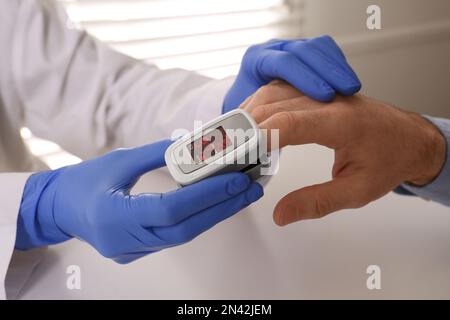 Arzt überprüft Sauerstoffgehalt des Patienten mit dem Pulsoxymeter am hellgrauen Tisch, Nahaufnahme Stockfoto