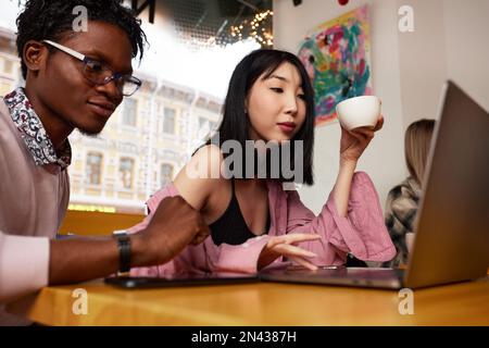 Multirassische Freunde, Mädchen und Kerle, die Spaß haben, Kaffee trinken, Tee im Café trinken, glückliche, vielfältige junge Leute, die scherzen, zusammen sitzen Stockfoto