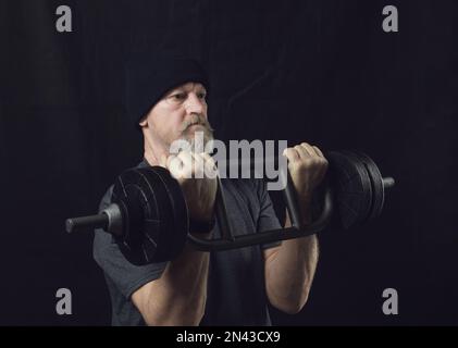 Aktiver älterer Mann mit Bart trainiert Bizeps mit einer Hantel. Stockfoto
