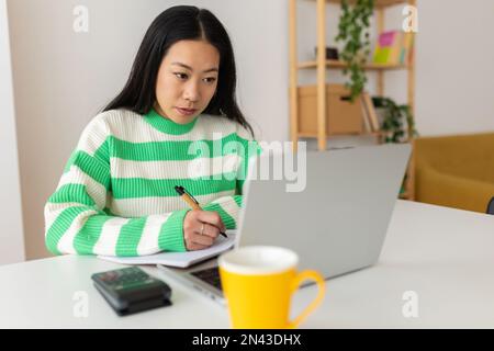 Junge asiatische Studentin, die mit einem Laptop zu Hause online lernt Stockfoto