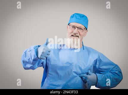 Infektionskrankheit Arzt mit grauem Bart in blauem Schutzanzug und Gummihandschuhen zeigt Daumen nach oben. Stockfoto