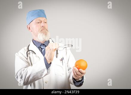Erfahrener älterer Ernährungsberater schaut sich eine orangefarbene Brille sorgfältig an. Stockfoto