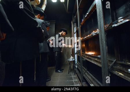 Junge Männer aus Chabad zünden eine Chanukkah Menorah in einem kleinen Raum im Ohel an, neben den Grabsteinen der letzten 2 Lubavitcher Rebbes. In Queens, New York City. Stockfoto