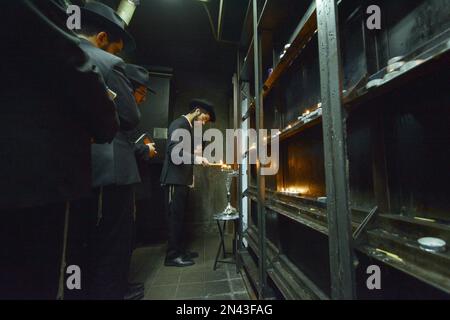 Junge Männer aus Chabad zünden eine Chanukkah Menorah in einem kleinen Raum im Ohel an, neben den Grabsteinen der letzten 2 Lubavitcher Rebbes. In Queens, New York City. Stockfoto