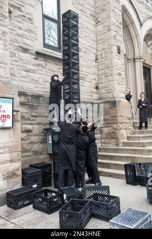 Ultraorthodoxe jüdische Jeschiva-Schüler in einer urbanen Schule verbringen Pause damit, einen Turm aus Milchkisten auf einem Bürgersteig zu bauen. In New York City. Stockfoto