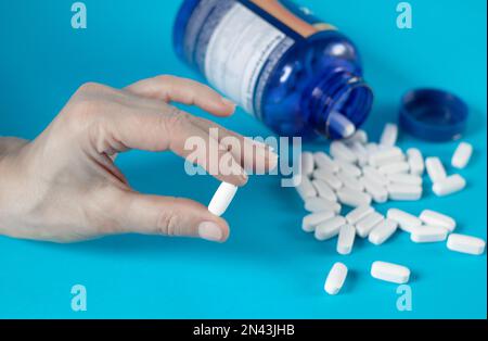 Weibliche Finger halten eine große weiße Pille mit Biozusätzen auf blauem Hintergrund. Stockfoto