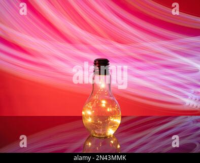 Weihnachtszubehör-Girlande aus LED-Glühbirnen in einer Glasflasche auf einem roten abstrakten Hintergrund. Stockfoto