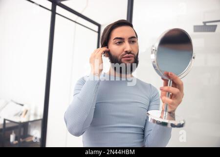 Fokussierter Transgender, der sein Aussehen nach der Make-up-Anwendung untersucht Stockfoto