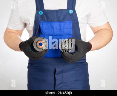 Ein Automechaniker hält zwei kaputte Wagenrollen vor dem Hintergrund eines blauen Overalls. Das Konzept des Austauschs rotierender Rollen in einem Pkw an einem Pkw Stockfoto