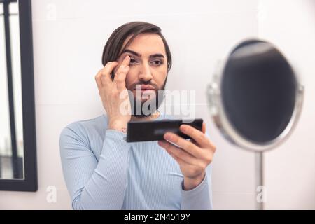 Fokussierter junger Mann, der Kosmetik auf sein Gesicht aufträgt Stockfoto