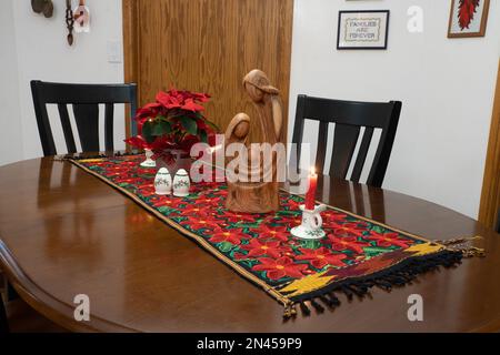 Weihnachtsdekorationen auf einem Tischläufer mit Poinsettia-Design in einem Haus in den USA. Im Preis inbegriffen ist eine Olivenholzschnitzerei von Mary, J. Stockfoto