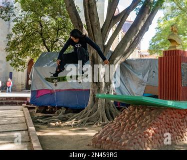 Ein junger mexikanischer Mann springt sein Skateboard vom Fuß einer Statue im El Llano Park in Oaxaca, Mexiko. Stockfoto
