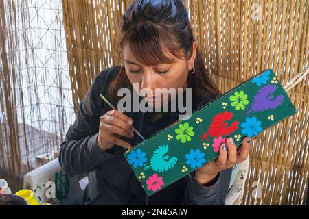 Ein Kunsthandwerker malt in einem Geschäft/einer Werkstatt in San Antonio Arrazola, Oaxaca, Mexiko, Designs auf eine Schachtel für eine Flasche Mescal. Stockfoto