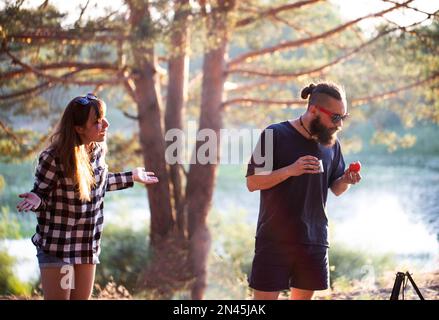 Das Mädchen spreizte ihre Arme an die Seiten und schwört auf einen Mann mit einem Bart in einer schwarzen Brille. Das Konzept eines Streits in einer Beziehung, Psychologie. Stockfoto