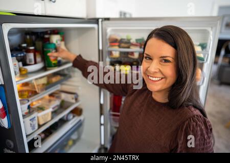 Essen aus dem Kühlschrank holen. Bier im Kühlschrank. Kühlschrank voller Essen. Gefrierschrank voll mit Essen. Eine Person, die entscheidet, was sie zum Abendessen von einem Freund essen Stockfoto