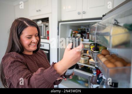 Essen aus dem Kühlschrank holen. Bier im Kühlschrank. Kühlschrank voller Essen. Gefrierschrank voll mit Essen. Eine Person, die entscheidet, was sie zum Abendessen von einem Freund essen Stockfoto