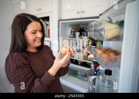 Essen aus dem Kühlschrank holen. Bier im Kühlschrank. Kühlschrank voller Essen. Gefrierschrank voll mit Essen. Eine Person, die entscheidet, was sie zum Abendessen von einem Freund essen Stockfoto