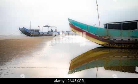 Traditionelle hölzerne Fischerboote, die bei Ebbe im Nebel am Strand von Tra Co in der Nähe von Mong Cai im Norden Vietnams gestrandet sind Stockfoto