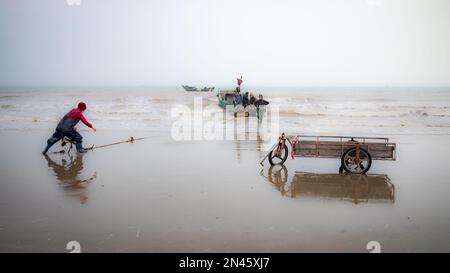 Eine Anglerfrau kämpft um den Anker, während sie sich bereit macht, vom Tra Co Beach in der Nähe von Mong Cai in Quang Ninh, Vietnam, zum Angeln aufzubrechen Stockfoto