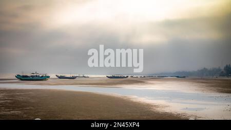 Traditionelle hölzerne Fischerboote, die bei Ebbe im Nebel am Strand von Tra Co in der Nähe von Mong Cai im Norden Vietnams gestrandet sind Stockfoto