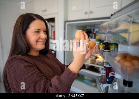 Essen aus dem Kühlschrank holen. Bier im Kühlschrank. Kühlschrank voller Essen. Gefrierschrank voll mit Essen. Eine Person, die entscheidet, was sie zum Abendessen von einem Freund essen Stockfoto