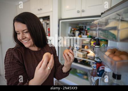 Essen aus dem Kühlschrank holen. Bier im Kühlschrank. Kühlschrank voller Essen. Gefrierschrank voll mit Essen. Eine Person, die entscheidet, was sie zum Abendessen von einem Freund essen Stockfoto