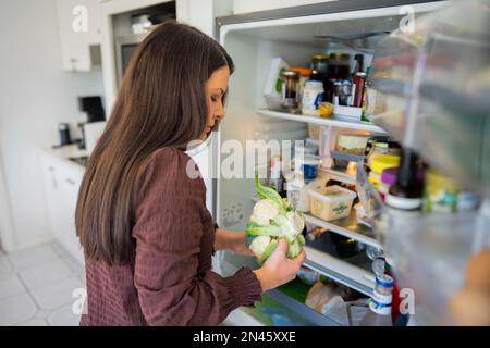 Essen aus dem Kühlschrank holen. Bier im Kühlschrank. Kühlschrank voller Essen. Gefrierschrank voll mit Essen. Eine Person, die entscheidet, was sie zum Abendessen von einem Freund essen Stockfoto