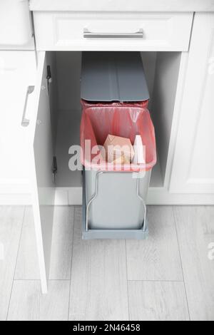 Offener Schrank mit vollem Mülleimer in der Küche Stockfoto