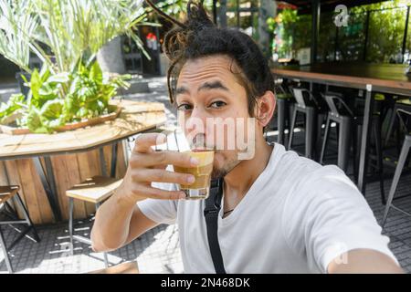 venezolanischer Latino-junger Mann mit Dreadlocks, der ein Selfie-Porträt macht, steht in einem Restaurant in argentinien und trinkt einen Latte, Getränke und Essen, Konzept C. Stockfoto