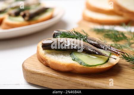 Köstliches Sandwich mit Sprotten, Gurken und Dill auf Holzbrett, Nahaufnahme Stockfoto