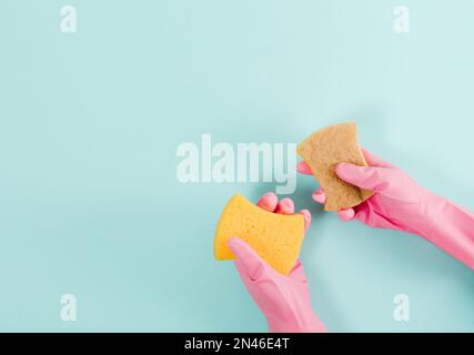 Hände in rosa Gummihandschuhen halten einen Waschschwamm. Blauer Hintergrund. Konzept der allgemeinen Ordnung und Sauberkeit. Flach verlegt Stockfoto