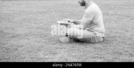 Zugeschnittenes Geschäftsmann mit Laptop zum Bloggen auf grünem Gras, Kopierplatz, Netzwerkadministrator Stockfoto