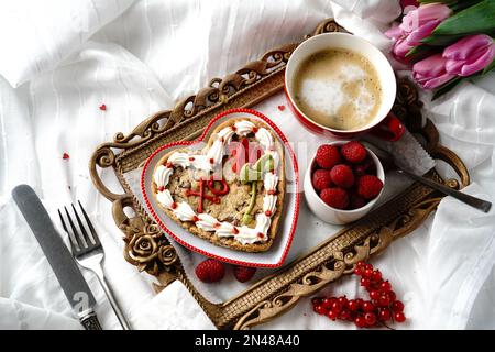 Frühstück im Bett mit herzförmigen Keksen Tasse Kaffee frische Himbeeren Johannisbeeren serviert in einem Tablett | Valentinstag Morgen Stockfoto