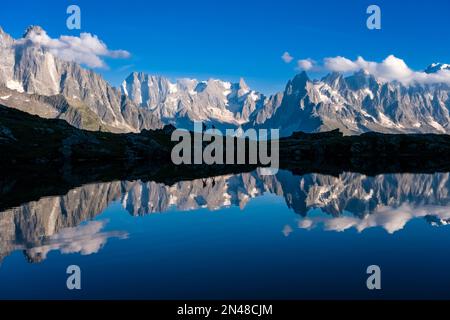 Die Gipfel des Mont Blanc-Massivs spiegeln sich auf der Oberfläche des Lacs des Chéserys wider, zwei Wanderer laufen auf einem Bergrücken in der Ferne. Stockfoto