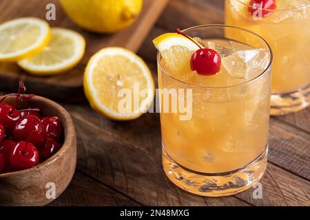 Whiskey Sour Cocktail mit Marachino-Kirsche und Zitronenscheibe auf rustikalem Holztisch Stockfoto