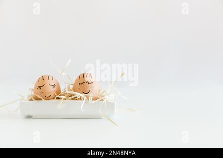 Braune handgezeichnete Eier mit Gesichtern im Nest. Ostern, Weihnachtskonzept, Geschenkgutschein für Ihr Design, Platz für Text. Weißer minimalistischer Hintergrund. Stockfoto