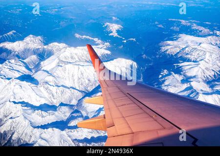 Flugzeug fliegt über Berggipfeln, die im Winter von Schnee bedeckt sind Stockfoto