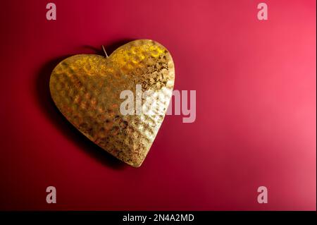 Goldfarbenes Herz aus Metall auf rotem Hintergrund, Valentinstag- oder Muttertagskarte, Liebessymbol, Kopierbereich, ausgewählter Fokus Stockfoto